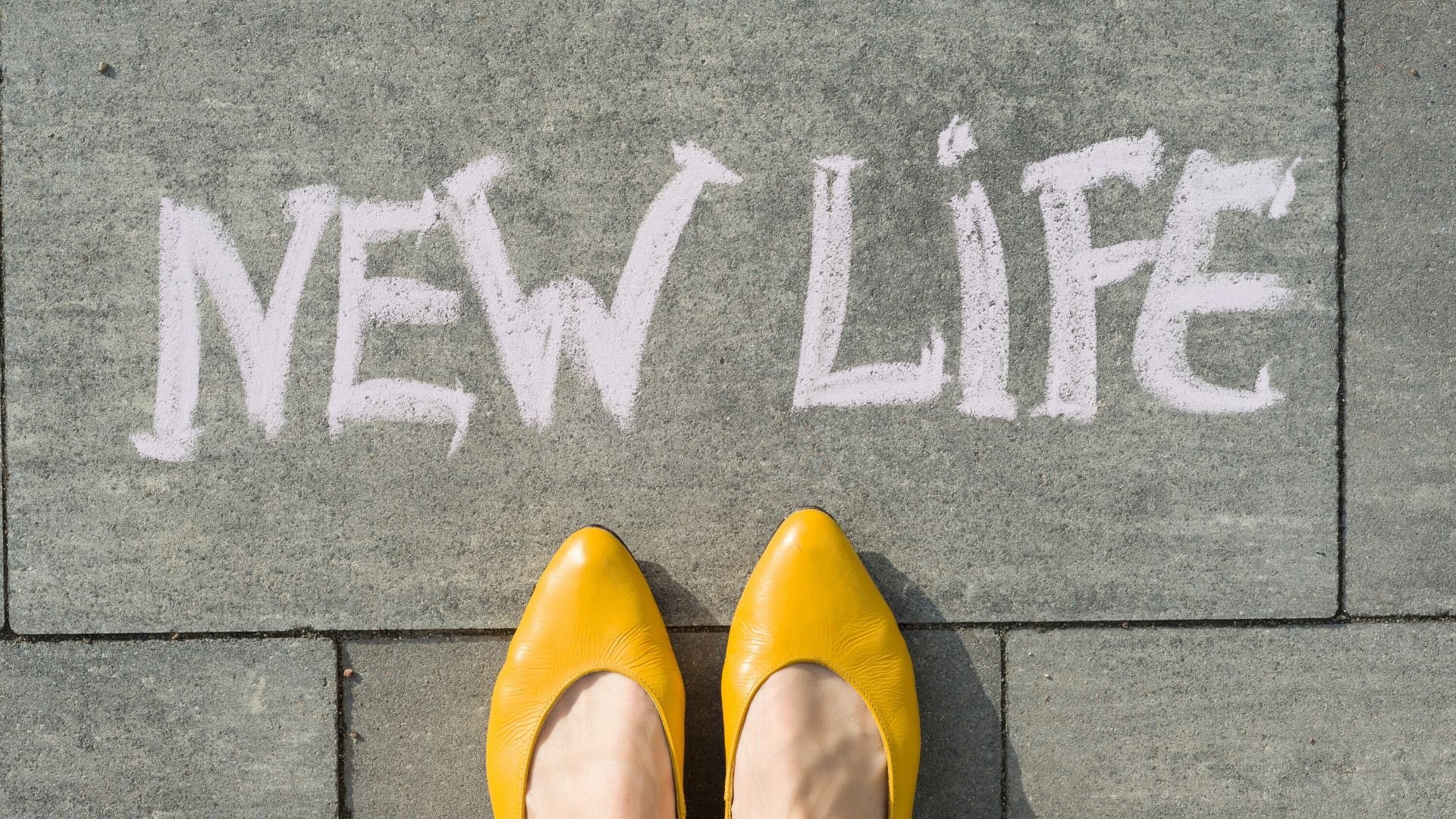 close up of someones feet wearing yellow hoes on a pavement with the words 'new life' written in chalk on the pavement