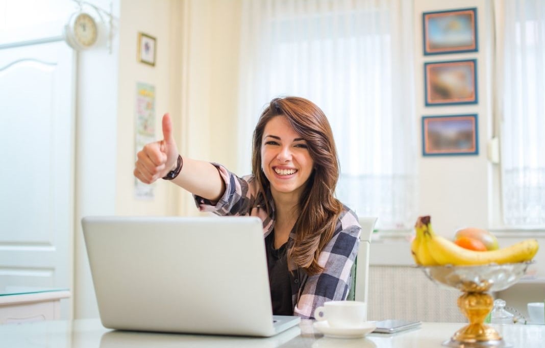 woman sitting at a desk with a laptop in front of her giving a thumbs up to the viewer