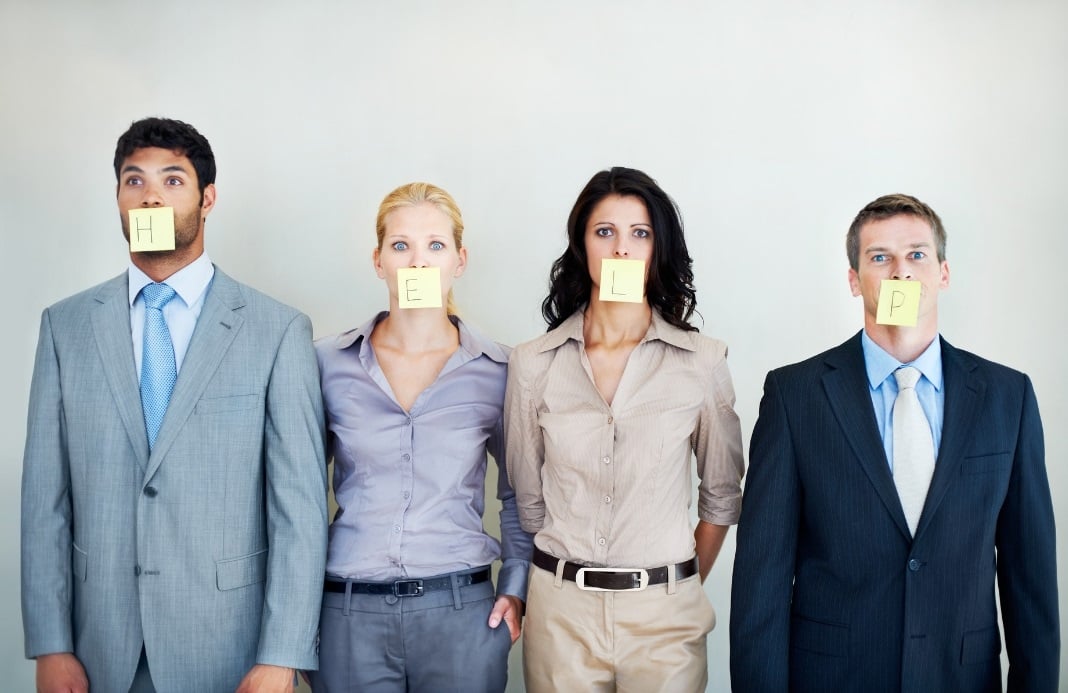 Two men and two women dressed in business atire looking straight ahead. Each with a post it note on their mouth spelling out the word help.