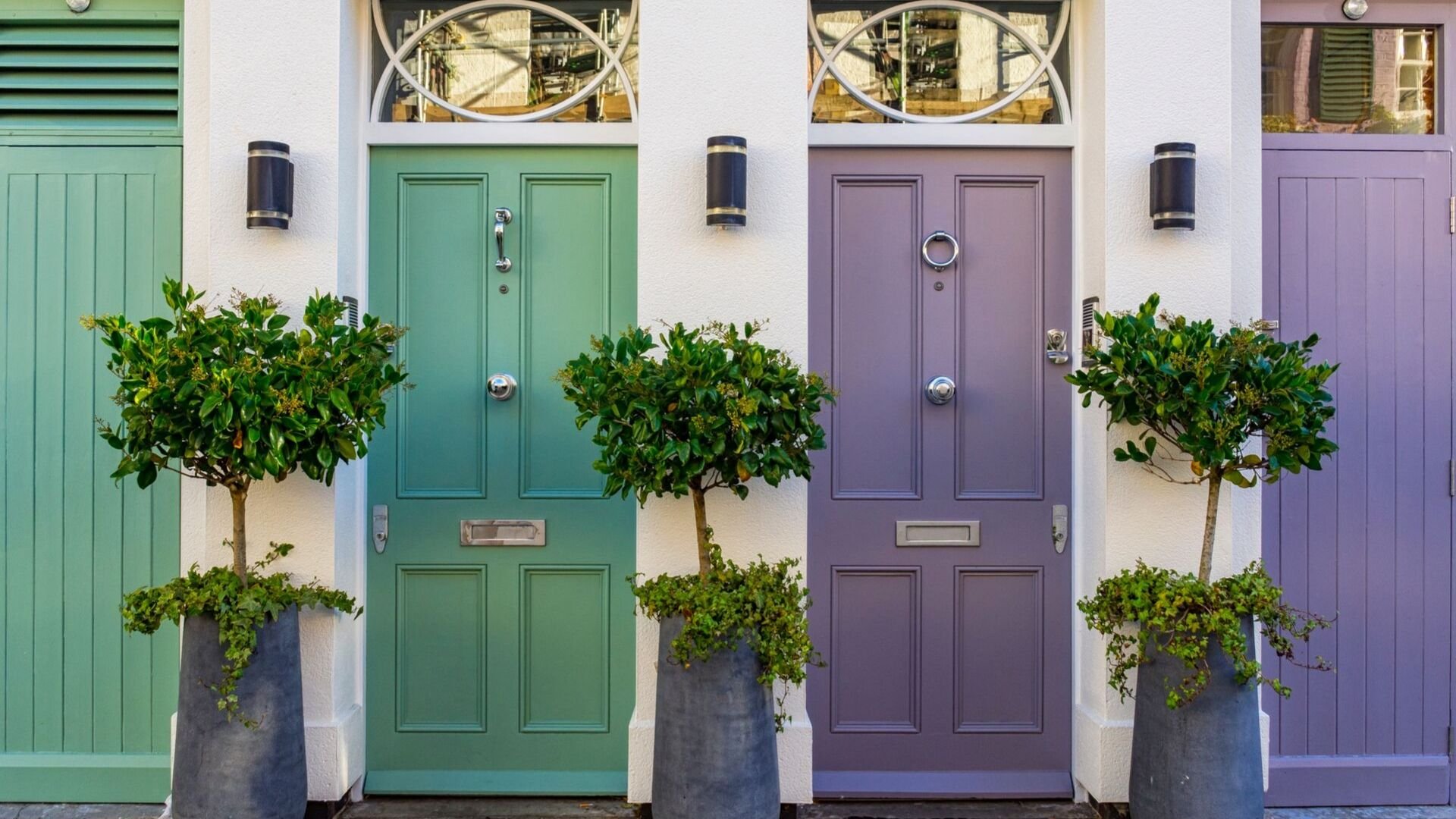 picture of two front doors, one has green paint and the lilac with bay trees either side of teh doors